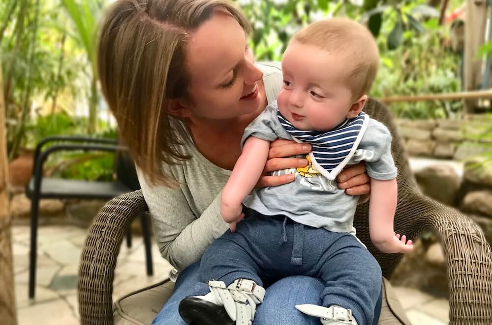 Sitting on Laura's lap, Ethan shows his arthrogryposis affected arms.